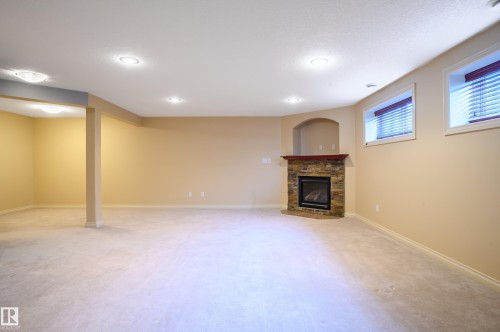 Basement featuring light colored carpet and a stone fireplace - 48 Fairway Point(E), Spruce Grove, AB - Indoor Photo Showing Basement With Fireplace