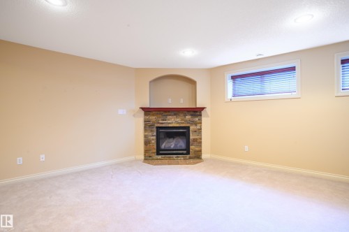 Unfurnished living room featuring light colored carpet and a stone fireplace - 48 Fairway Point(E), Spruce Grove, AB - Indoor With Fireplace