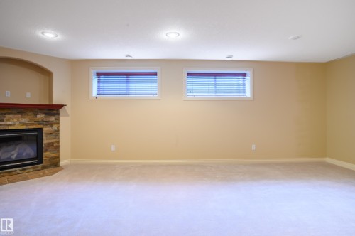 Unfurnished living room featuring light carpet, healthy amount of natural light, and a stone fireplace - 48 Fairway Point(E), Spruce Grove, AB - Indoor With Fireplace