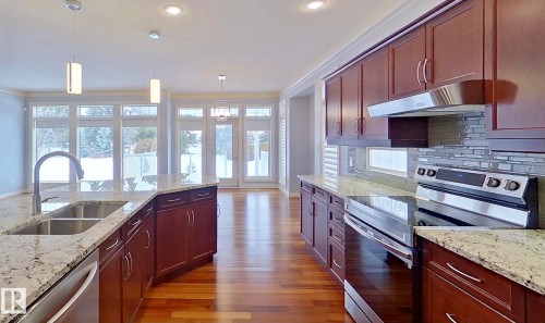 Kitchen with stainless steel appliances, light stone countertops, dark wood-type flooring, decorative light fixtures, and backsplash - 48 Fairway Point(E), Spruce Grove, AB - Indoor Photo Showing Kitchen With Double Sink With Upgraded Kitchen