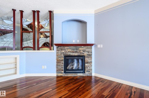 Unfurnished living room featuring built in features, a stone fireplace, wood finished floors, and a textured ceiling - 48 Fairway Point(E), Spruce Grove, AB - Indoor Photo Showing Living Room With Fireplace