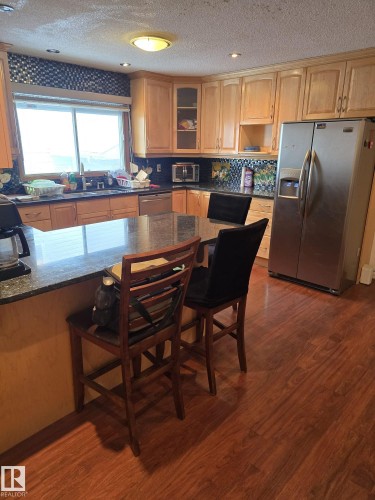 Kitchen with a breakfast bar area, stainless steel appliances, dark wood-type flooring, dark stone counters, and a textured ceiling - 11927 85 Street Nw, Edmonton, AB - Indoor