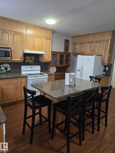 Kitchen with a kitchen breakfast bar, decorative backsplash, white appliances, a center island, and glass insert cabinets - 11927 85 Street Nw, Edmonton, AB - Indoor Photo Showing Kitchen