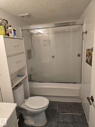 Bathroom featuring vanity, a textured ceiling, combined bath / shower with glass door, and dark tile patterned floors - 11927 85 Street Nw, Edmonton, AB - Indoor Photo Showing Bathroom