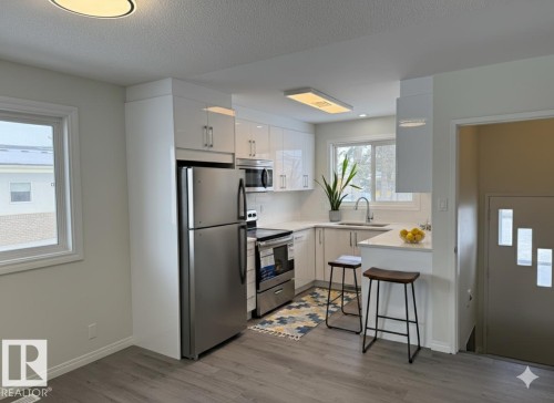 Virtually staged Kitchen with stainless steel appliances, white cabinets, light LVP and a peninsula - 13323 68 Street, Edmonton, AB - Indoor Photo Showing Kitchen