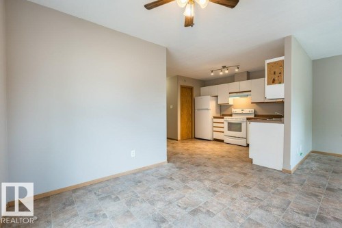 Kitchen with stone finish flooring, white appliances, a ceiling fan, white cabinets, and dark countertops - 4827 54 Avenue, Wetaskiwin, AB - Indoor Photo Showing Kitchen