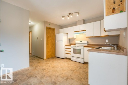 Kitchen with white appliances, stone finish flooring, white cabinets, and light countertops - 4827 54 Avenue, Wetaskiwin, AB - Indoor Photo Showing Kitchen With Double Sink