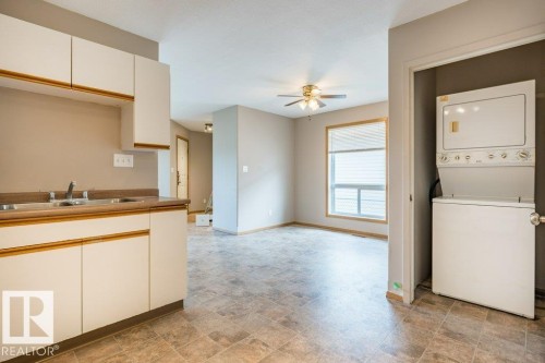 Two tone kitchen featuring stone finish flooring, a ceiling fan, stacked washer and dryer, and dual tone cabinetry - 4827 54 Avenue, Wetaskiwin, AB - Indoor Photo Showing Laundry Room