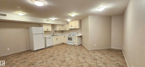 Kitchen featuring stone finish floors, white appliances, light countertops, a textured ceiling, and white cabinets - 4827 54 Avenue, Wetaskiwin, AB - Indoor Photo Showing Kitchen With Double Sink