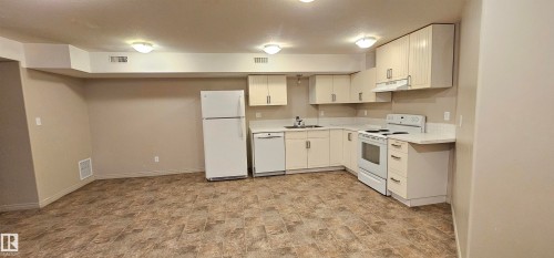 Kitchen featuring stone finish flooring, white appliances, light countertops, white cabinets, and a textured ceiling - 4827 54 Avenue, Wetaskiwin, AB - Indoor Photo Showing Kitchen