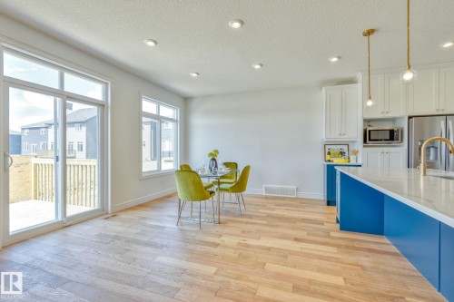 Kitchen featuring dual tone cabinetry, stainless steel appliances, hanging light fixtures, a textured ceiling, and light wood finished floors - 8320 Mayday Link Sw, Edmonton, AB - Indoor