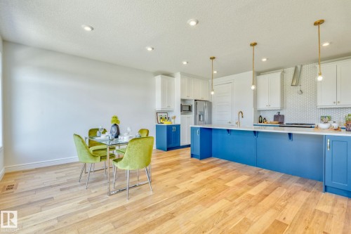 Kitchen featuring two tone cabinetry, a breakfast bar, light wood-style flooring, decorative light fixtures, and stainless steel appliances - 8320 Mayday Link Sw, Edmonton, AB - Indoor Photo Showing Other Room