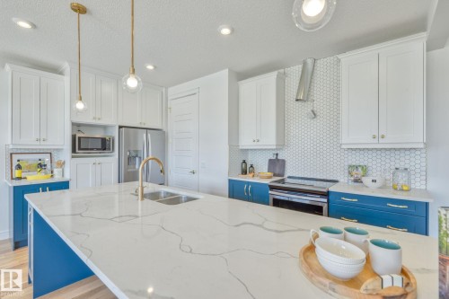 Kitchen featuring two tone cabinets, decorative backsplash, stainless steel appliances, light wood-style flooring, and hanging light fixtures - 8320 Mayday Link Sw, Edmonton, AB - Indoor Photo Showing Kitchen With Double Sink With Upgraded Kitchen