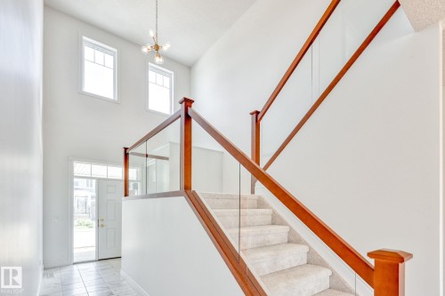 Staircase with hanging lights, a high ceiling, and marble look tile flooring - 8320 Mayday Link Sw, Edmonton, AB - Indoor Photo Showing Other Room