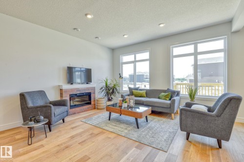 Living area with a fireplace, light wood-style flooring, a textured ceiling, and recessed lighting - 8320 Mayday Link Sw, Edmonton, AB - Indoor Photo Showing Living Room With Fireplace