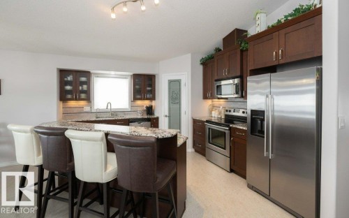 Kitchen with stainless steel appliances, glass fronted cabinets, light stone counters, tasteful backsplash, and a kitchen breakfast bar - 11116 103 Street, Westlock, AB - Indoor