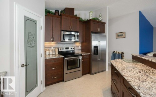 Kitchen featuring stainless steel appliances, light stone countertops, dark wood finish cabinetry, and decorative backsplash - 11116 103 Street, Westlock, AB - Indoor Photo Showing Kitchen With Stainless Steel Kitchen
