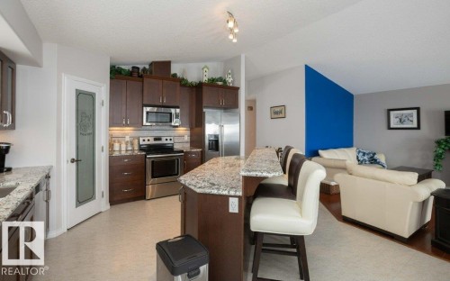 Kitchen with open floor plan, stainless steel appliances, dark wood finish cabinetry, light stone counters, and a kitchen bar - 11116 103 Street, Westlock, AB - Indoor Photo Showing Kitchen With Stainless Steel Kitchen
