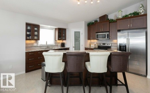 Kitchen with dark wood finish cabinetry, stainless steel appliances, a kitchen breakfast bar, glass fronted cabinets, and lofted ceiling - 11116 103 Street, Westlock, AB - Indoor