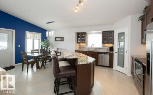 Kitchen with glass fronted cabinets, light stone counters, a breakfast bar, stainless steel appliances, and light flooring - 11116 103 Street, Westlock, AB - Indoor