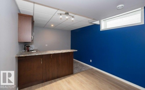 Indoor wet bar featuring dark wood finish cabinetry, light stone countertops, light wood finished floors, and a drop ceiling - 11116 103 Street, Westlock, AB - Indoor Photo Showing Other Room