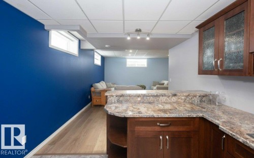 Bar with glass insert cabinets, a paneled ceiling, light wood-style floors, light stone counters, and dark wood finish cabinetry - 11116 103 Street, Westlock, AB - Indoor