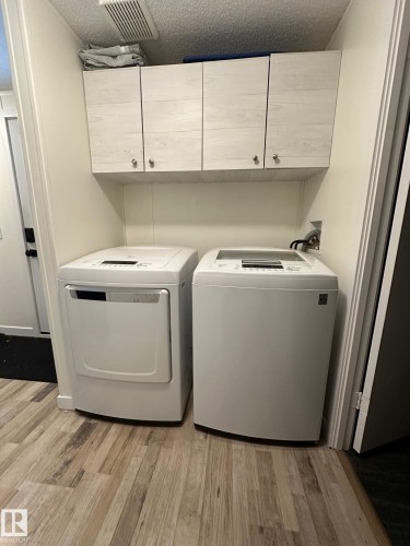 Laundry area featuring a textured ceiling, light wood-style flooring, washer and dryer, and cabinet space - 341 West Brook Way Nw, Edmonton, AB - Indoor Photo Showing Laundry Room