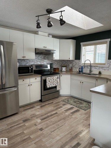 Kitchen featuring a skylight, stainless steel appliances, white cabinetry, a textured ceiling, and backsplash - 341 West Brook Way Nw, Edmonton, AB - Indoor Photo Showing Kitchen With Double Sink