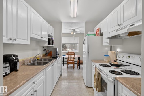 Kitchen featuring white appliances, white cabinetry, light countertops, and ceiling fan - 302 4608 52 Avenue, Stony Plain, AB - Indoor Photo Showing Kitchen With Double Sink