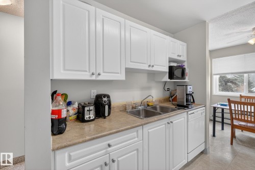 Kitchen featuring a textured ceiling, white cabinetry, light countertops, white dishwasher, and black microwave - 302 4608 52 Avenue, Stony Plain, AB - Indoor Photo Showing Kitchen With Double Sink