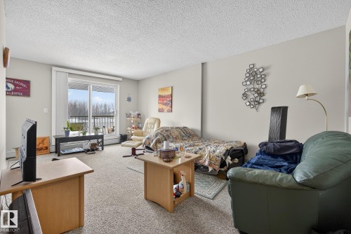 Living area with light colored carpet and a textured ceiling - 302 4608 52 Avenue, Stony Plain, AB - Indoor Photo Showing Other Room