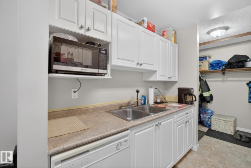Kitchen featuring stainless steel microwave, white cabinetry, dishwasher, and light countertops - 307 4608 52 Avenue, Stony Plain, AB - Indoor Photo Showing Kitchen With Double Sink