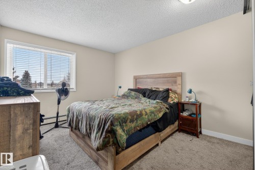 Bedroom with light carpet, a baseboard radiator, and a textured ceiling - 307 4608 52 Avenue, Stony Plain, AB - Indoor Photo Showing Bedroom