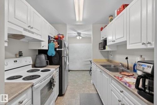 Kitchen with white appliances, white cabinets, and light countertops - 307 4608 52 Avenue, Stony Plain, AB - Indoor Photo Showing Kitchen With Double Sink