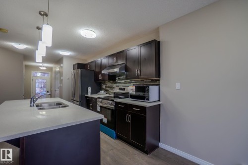 Kitchen featuring decorative light fixtures, stainless steel appliances, backsplash, a center island with sink, and a textured ceiling - Edmonton, AB - Indoor Photo Showing Kitchen With Double Sink