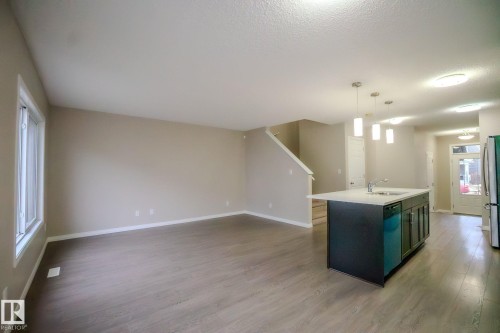 Kitchen with an island with sink, decorative light fixtures, light wood-style floors, open floor plan, and a textured ceiling - Edmonton, AB - Indoor Photo Showing Kitchen