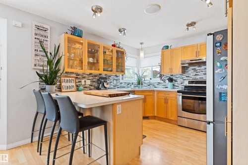 Kitchen with glass fronted cabinets, a peninsula, light countertops, stainless steel appliances, and a breakfast bar - 7804 Schmid Place, Edmonton, AB - Indoor Photo Showing Kitchen With Double Sink