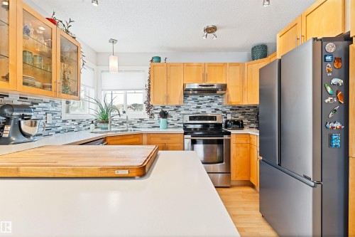 Kitchen with stainless steel appliances, decorative light fixtures, light wood-type flooring, light wood finish cabinets, and glass insert cabinets - 7804 Schmid Place, Edmonton, AB - Indoor Photo Showing Kitchen With Double Sink