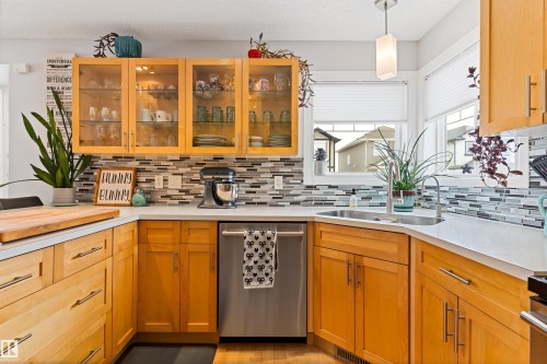 Kitchen featuring stainless steel dishwasher, decorative light fixtures, glass fronted cabinets, decorative backsplash, and a textured ceiling - 7804 Schmid Place, Edmonton, AB - Indoor Photo Showing Kitchen With Double Sink