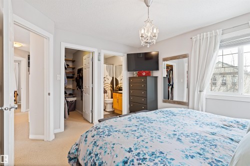 Bedroom featuring a walk in closet, a chandelier, light colored carpet, a textured ceiling, and ensuite bathroom - 7804 Schmid Place, Edmonton, AB - Indoor Photo Showing Bedroom