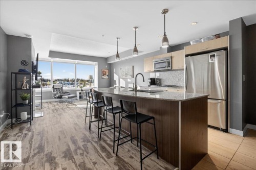 Kitchen with dark stone countertops, stainless steel appliances, decorative light fixtures, a kitchen bar, and light wood finish cabinets - 301 2504 109 Street, Edmonton, AB - Indoor Photo Showing Kitchen With Upgraded Kitchen