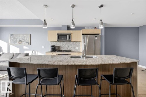 Kitchen with light stone counters, stainless steel appliances, pendant lighting, backsplash, and a kitchen breakfast bar - 301 2504 109 Street, Edmonton, AB - Indoor Photo Showing Kitchen With Double Sink With Upgraded Kitchen