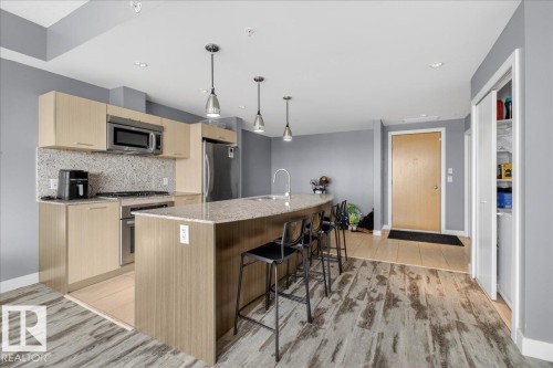 Kitchen with light wood finish cabinetry, light stone counters, decorative light fixtures, stainless steel appliances, and a kitchen bar - 301 2504 109 Street, Edmonton, AB - Indoor Photo Showing Kitchen With Upgraded Kitchen