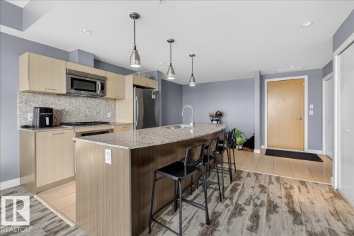 Kitchen with light stone countertops, light wood finish cabinets, backsplash, stainless steel appliances, and decorative light fixtures - 301 2504 109 Street, Edmonton, AB - Indoor Photo Showing Kitchen With Upgraded Kitchen