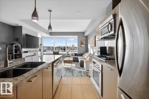 Kitchen with stainless steel appliances, open floor plan, decorative light fixtures, light stone counters, and light wood finish cabinetry - 301 2504 109 Street, Edmonton, AB - Indoor Photo Showing Kitchen With Double Sink With Upgraded Kitchen