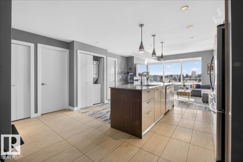 Kitchen featuring stacked washing machine and dryer, dark stone counters, decorative light fixtures, a center island with sink, and modern cabinets - 301 2504 109 Street, Edmonton, AB - Indoor Photo Showing Kitchen
