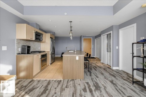 Kitchen with a center island with sink, pendant lighting, a breakfast bar area, light wood finish cabinets, and stainless steel appliances - 301 2504 109 Street, Edmonton, AB - Indoor Photo Showing Kitchen