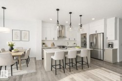 Kitchen featuring stainless steel appliances, a kitchen bar, light wood finished floors, white cabinetry, and a kitchen island with sink - 