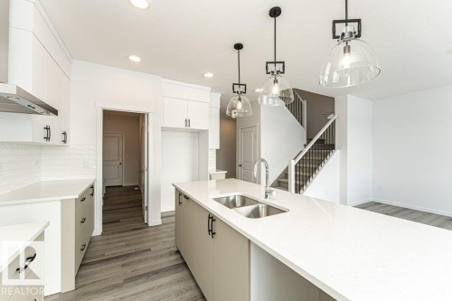 Kitchen featuring light wood finished floors, decorative light fixtures, light stone counters, and tasteful backsplash - 3790 Wren Loop, Edmonton, AB - Indoor Photo Showing Kitchen With Double Sink With Upgraded Kitchen