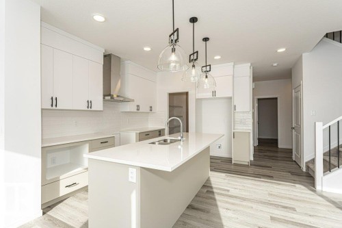 Kitchen with a center island with sink, backsplash, white cabinetry, light wood-type flooring, and light stone counters - 3790 Wren Loop, Edmonton, AB - Indoor Photo Showing Kitchen With Double Sink With Upgraded Kitchen